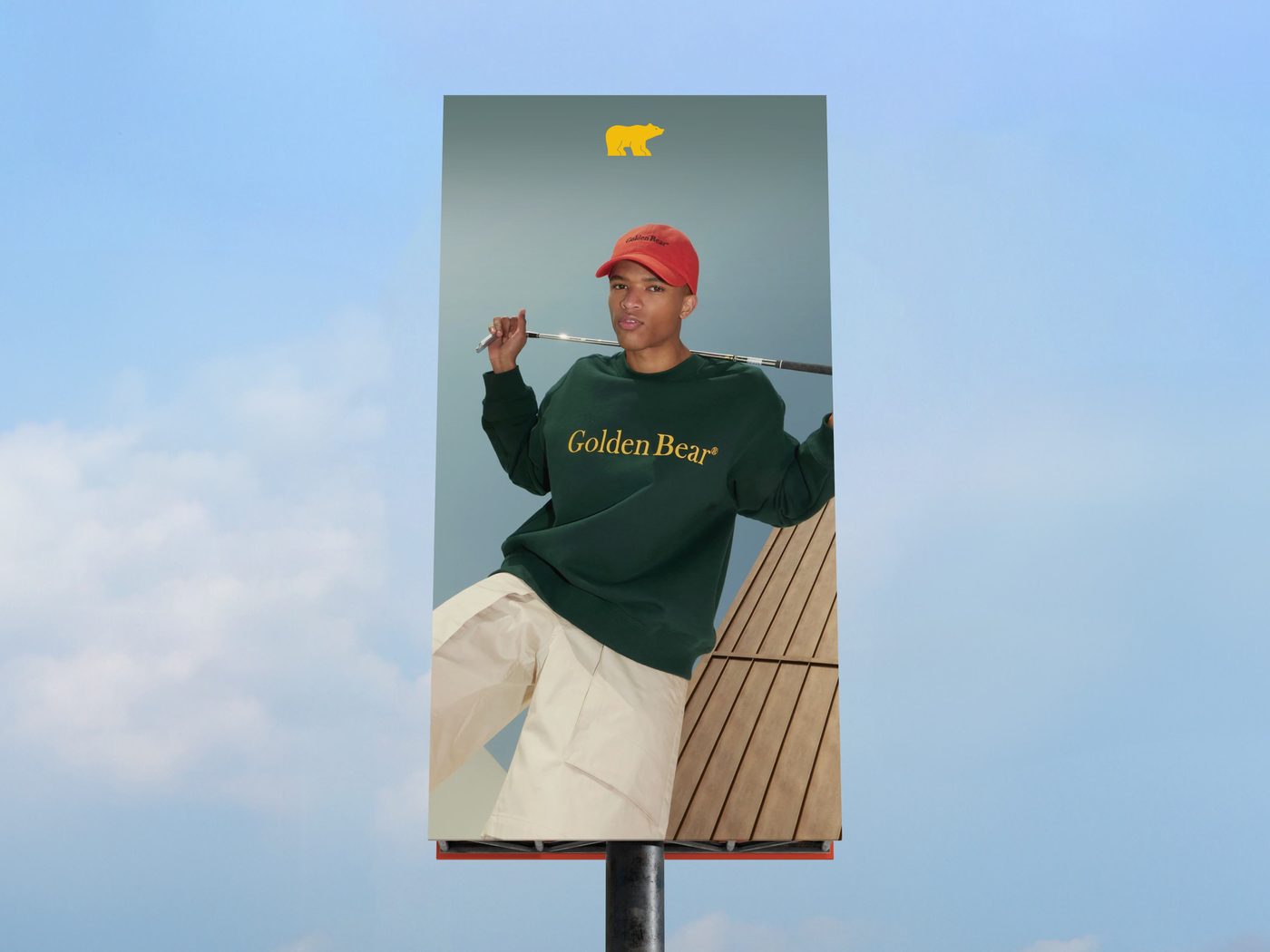 Golden Bear billboard against a blue sky: man in a forest green crewneck raising a club, red cap on