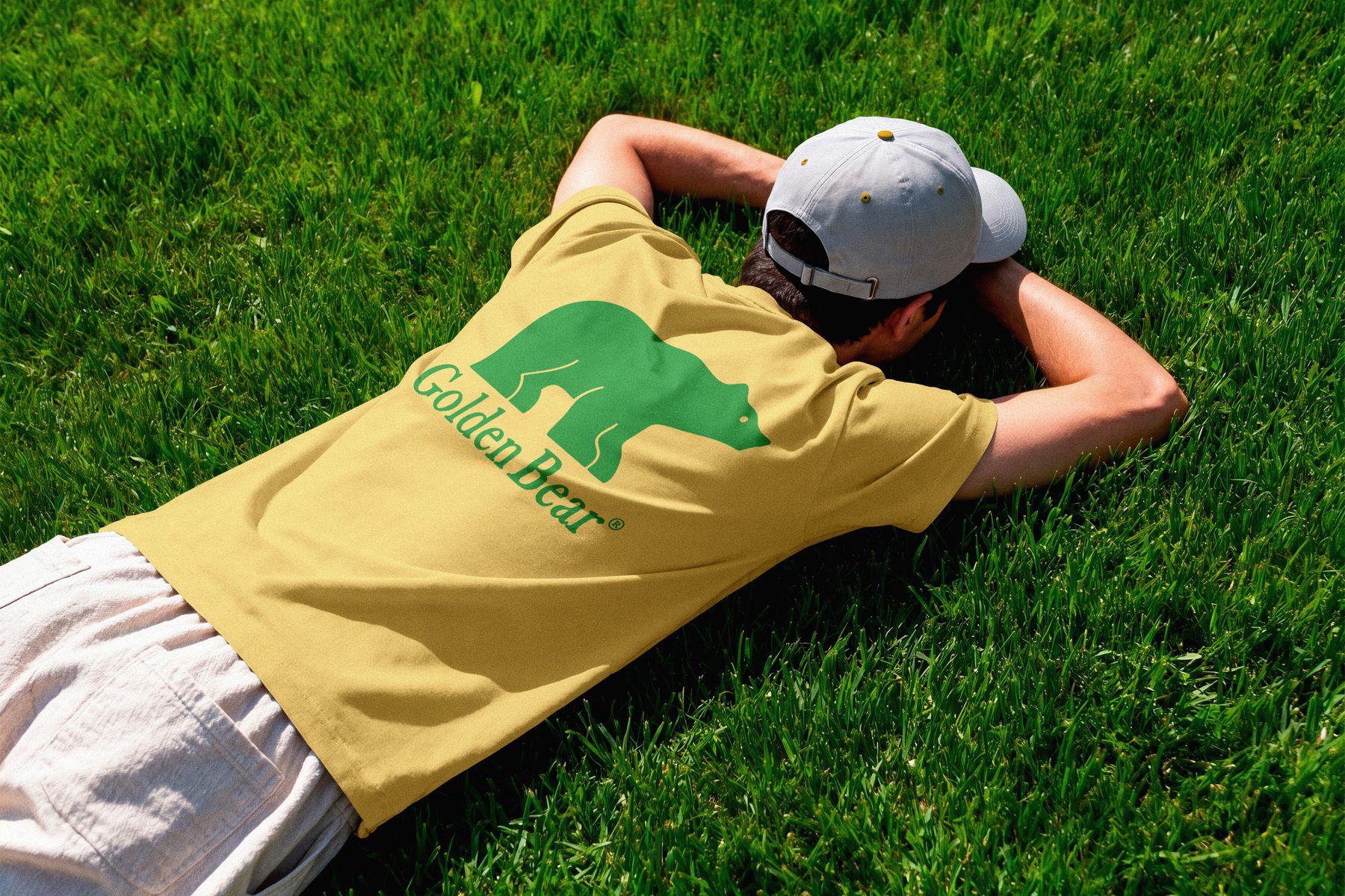 Man lying on course grass in a golden yellow tee with a large green Golden Bear graphic on the back