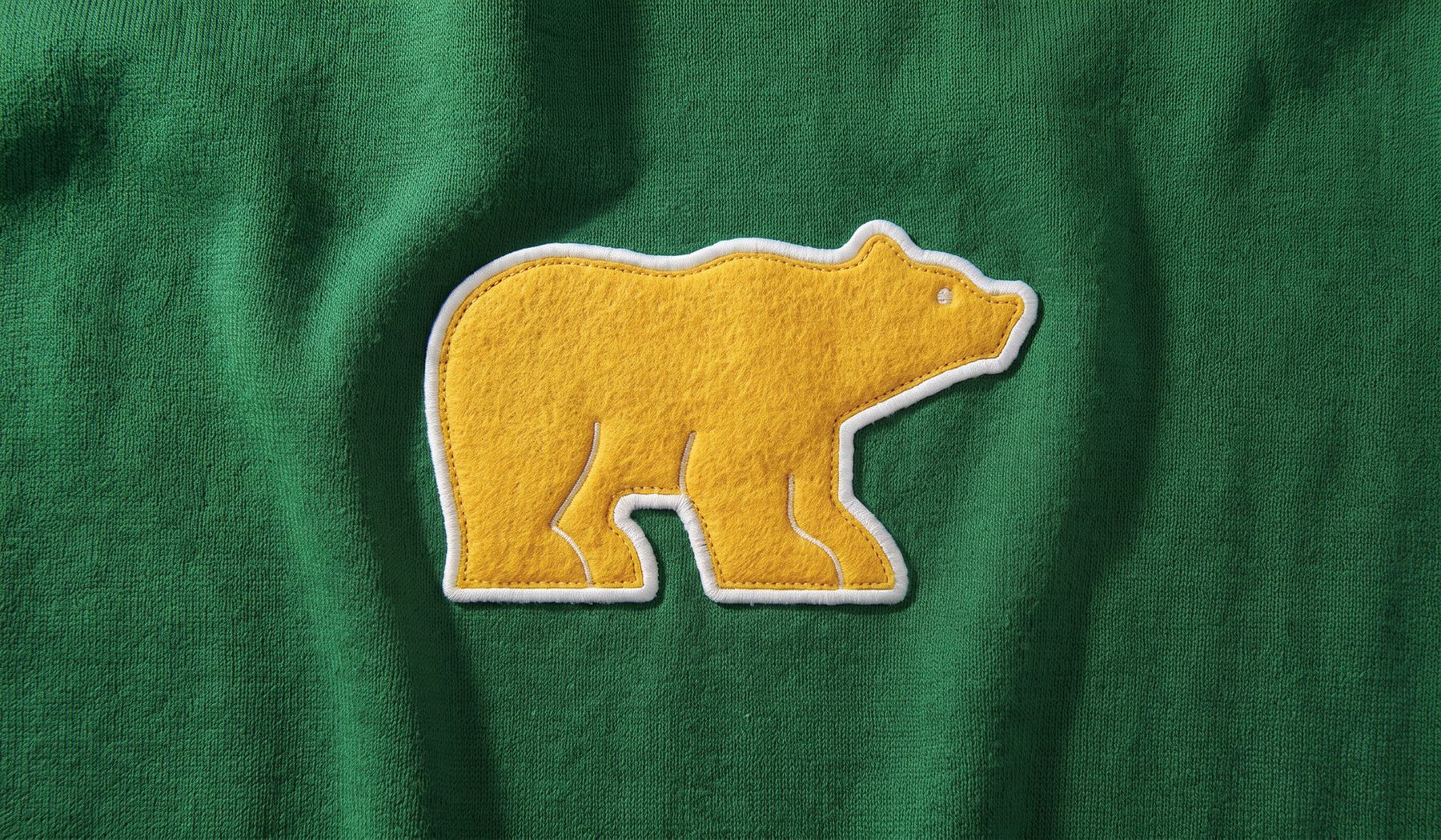 Close-up of the gold Golden Bear chenille patch stitched on kelly green French terry