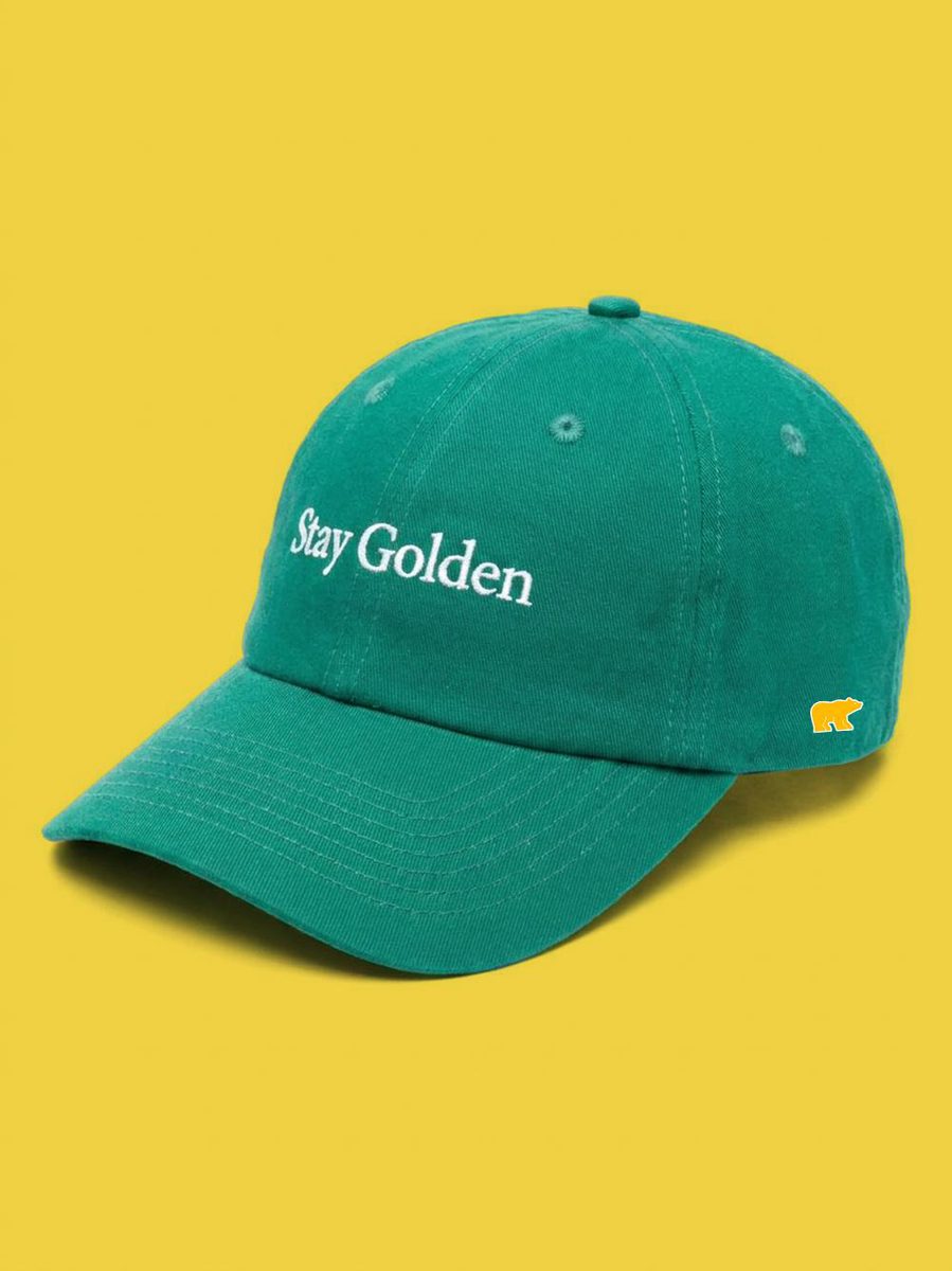 Kelly green canvas dad cap with white Stay Golden embroidery, on a yellow background